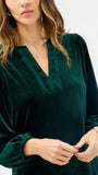 Woman wearing a festive green velvet long sleeve short dress with a tiered skirt on a white background