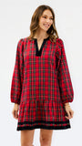 A woman modeling a red tartan plaid mini dress with black velvet trim at the split neckline and hem, set against a plain white studio background.