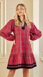A woman modeling a red tartan plaid nightgown with black trim, standing in a brightly lit room with cream-colored columns and a window.