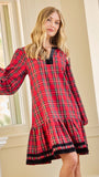 A woman wearing a red and black plaid long-sleeve nightgown with a tiered hem, posing indoors near a window.