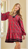 A woman wearing a red and black plaid long-sleeve nightgown or tunic dress, posing in front of a white classical column and window.