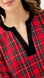 A close-up of a woman wearing a red tartan plaid top with a contrasting black velvet V-neck trim.