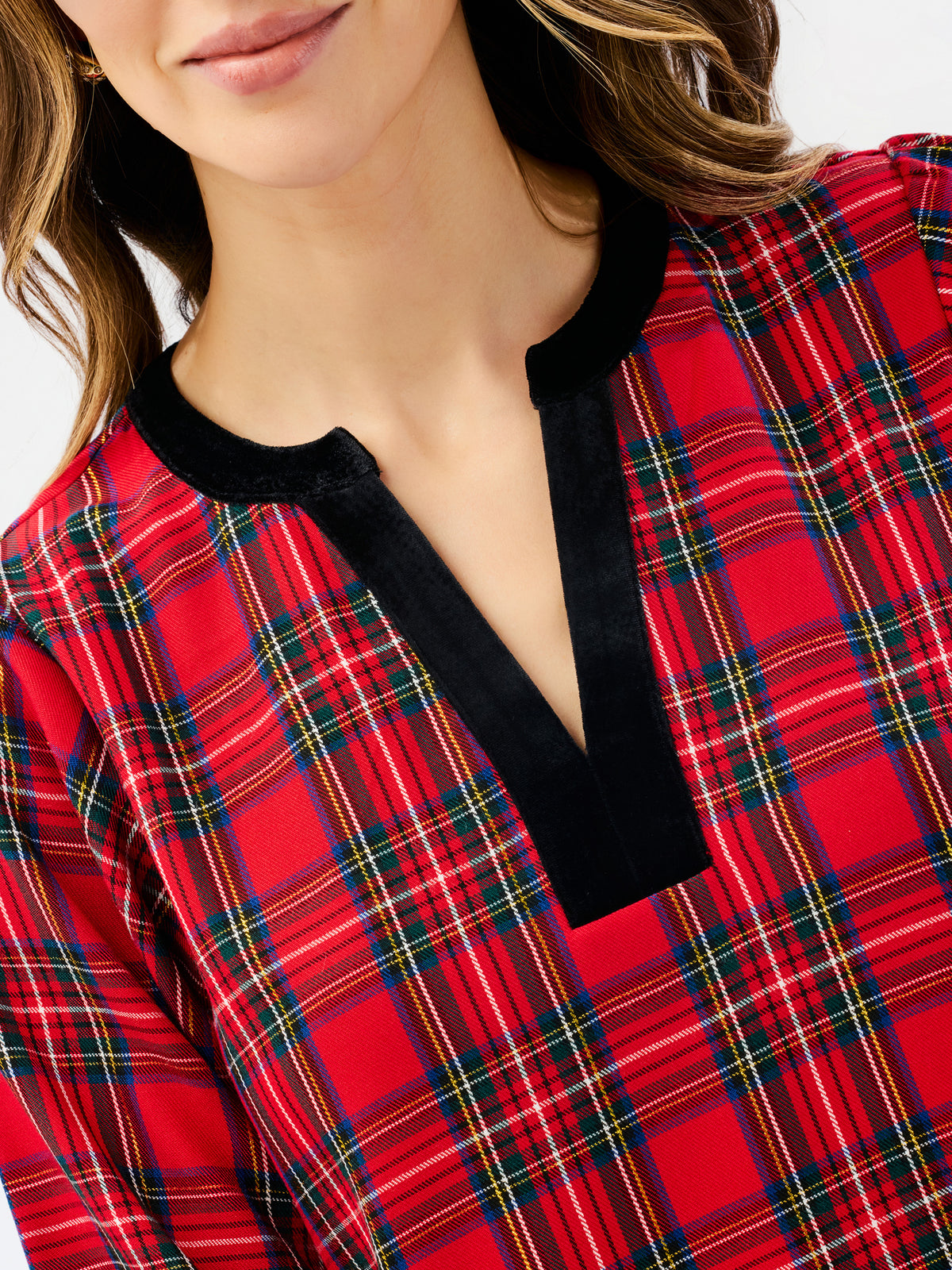 A close-up of a woman wearing a red tartan plaid top with a contrasting black velvet V-neck trim.