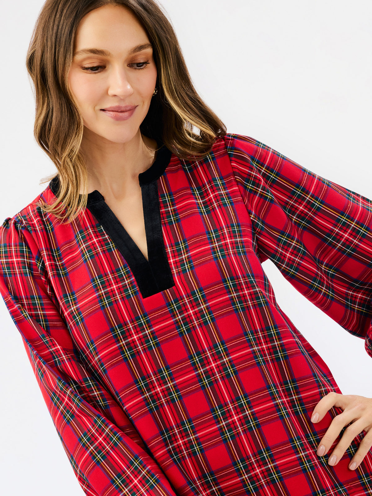 A woman wearing a red plaid long-sleeve top with a black V-neck trim, shown against a plain light gray studio background.
