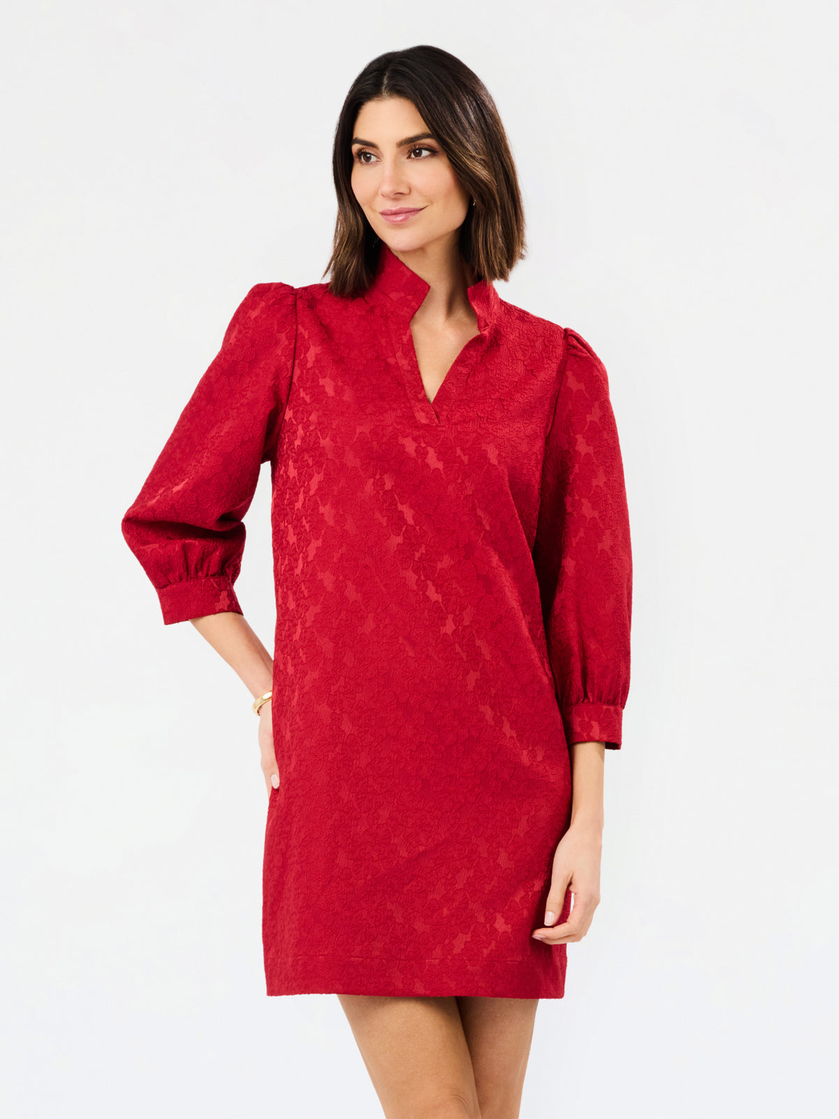 A woman modeling a red textured mini dress with three-quarter puff sleeves and a split neckline, photographed against a plain white studio background.