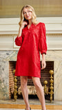 A woman modeling a bright red textured midi dress with three-quarter sleeves, standing in front of an ornate fireplace.
