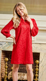 A woman wearing a bright red lace long-sleeve tunic dress stands in front of an ornate fireplace with marble and gold accents.