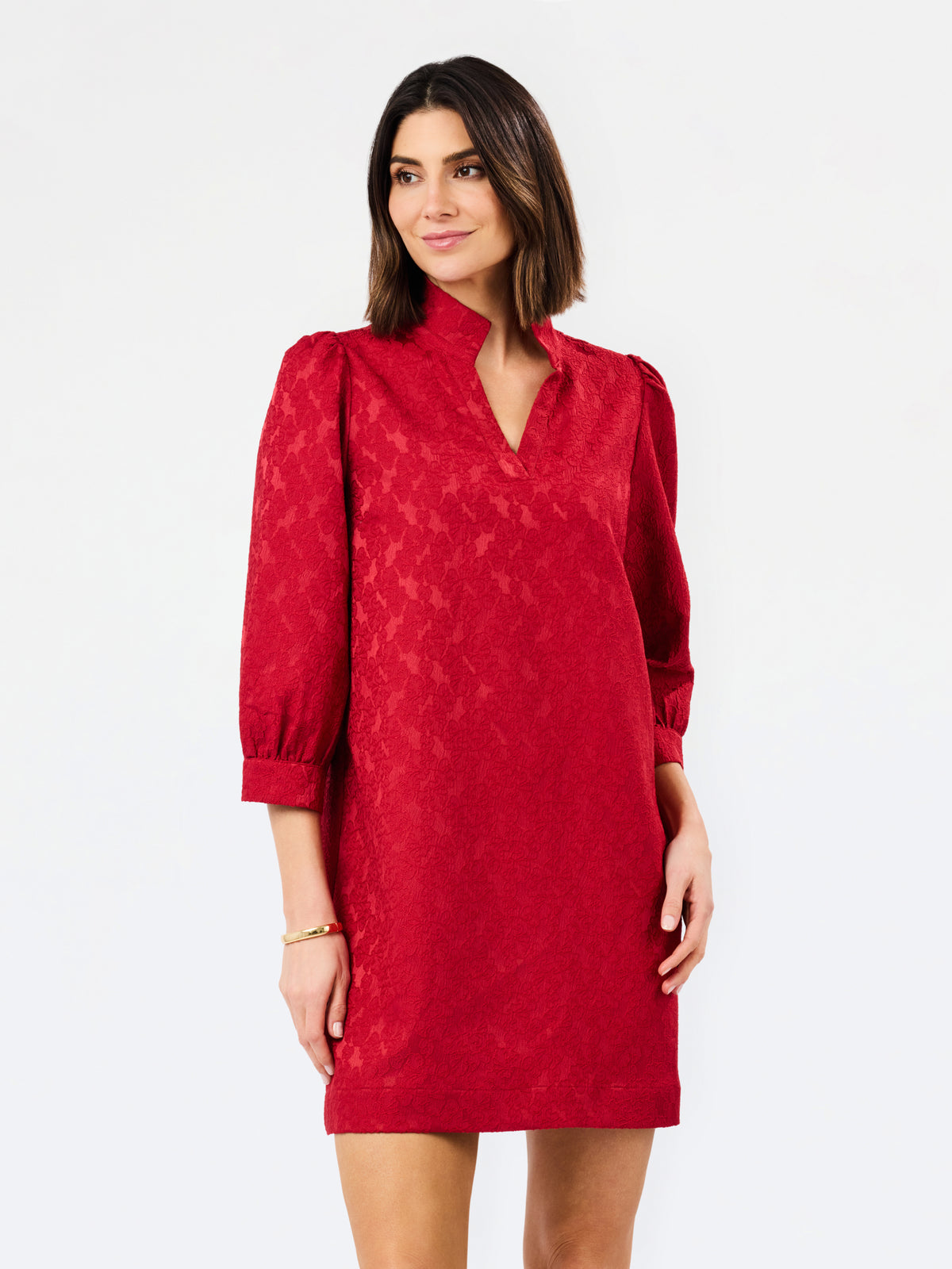 A woman modeling a red textured dress with three-quarter puffed sleeves and a split neckline, photographed against a plain white studio background.