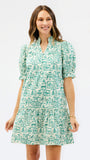 A woman modeling a short puff-sleeve dress with a green and white architectural line-art print, set against a plain white studio background.