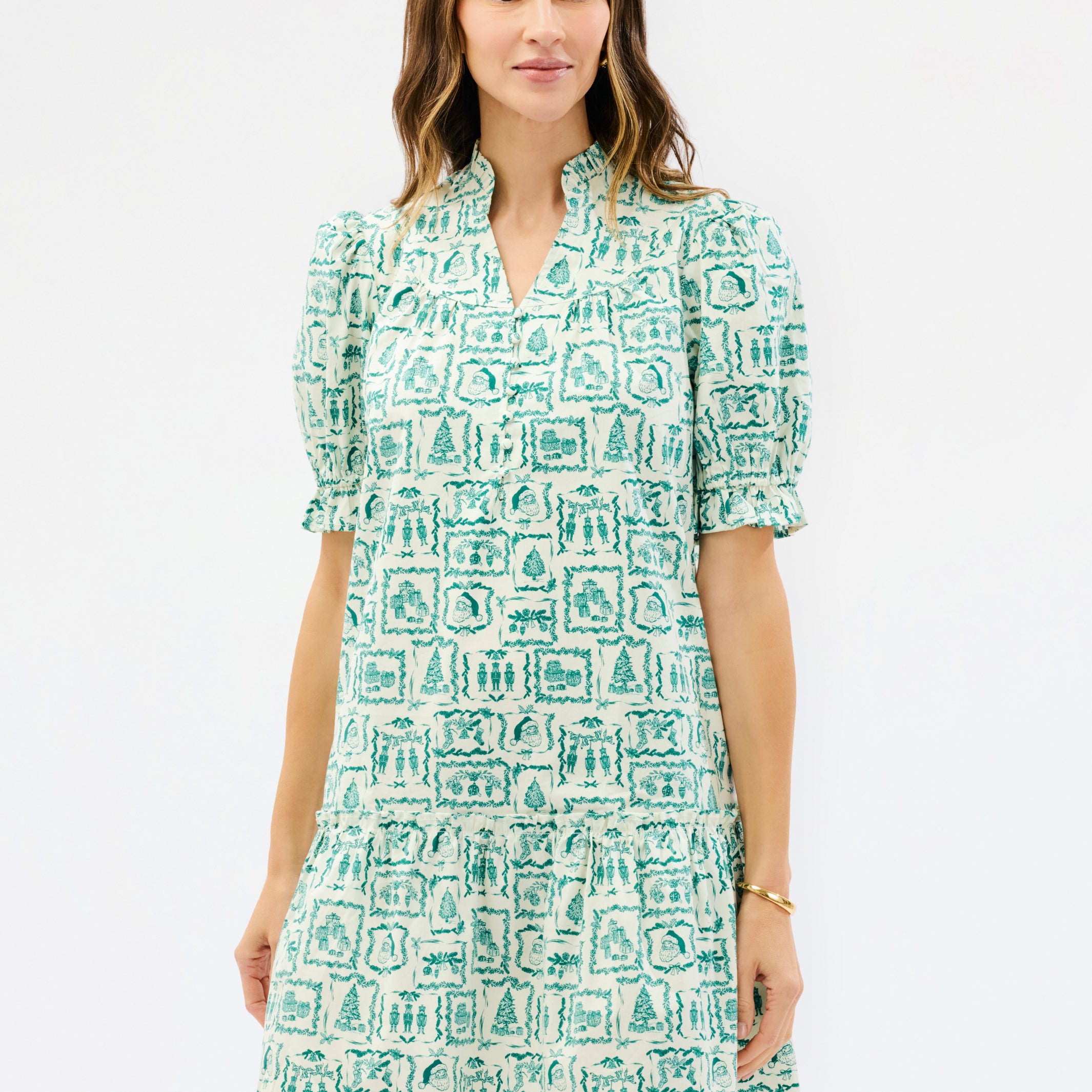 A woman modeling a short-sleeve V-neck dress with puff sleeves and an allover green and white architectural block print, set against a plain white studio background.