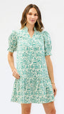 A woman modeling a short-sleeve V-neck dress with puff sleeves and an allover green and white graphic print, set against a plain white studio background.