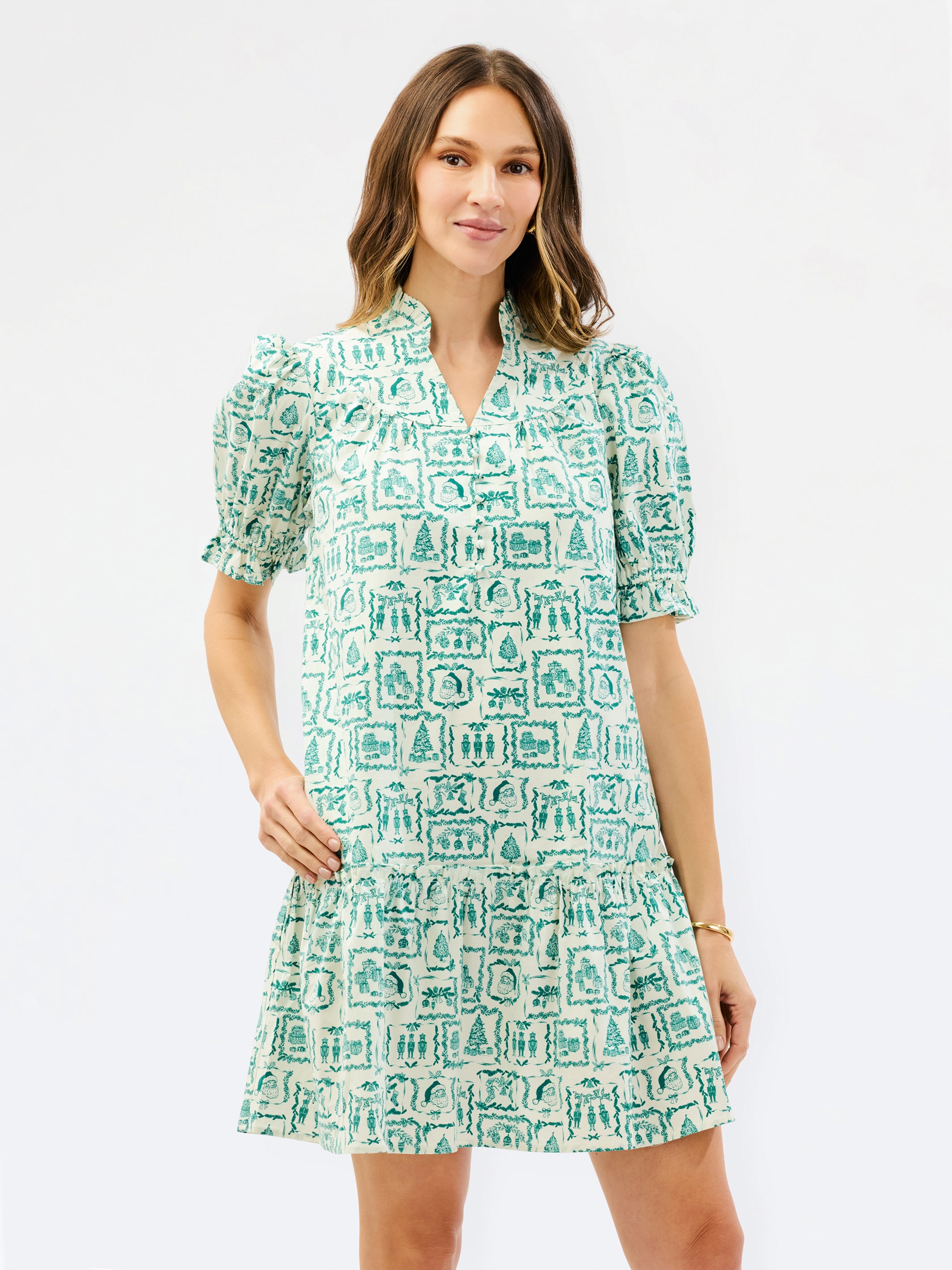A woman modeling a short-sleeve V-neck dress with puff sleeves and an allover green and white graphic print, set against a plain white studio background.