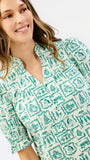 A woman wearing a short-sleeve button-up shirt with a green and white hand-drawn style pattern, photographed against a clean white background.
