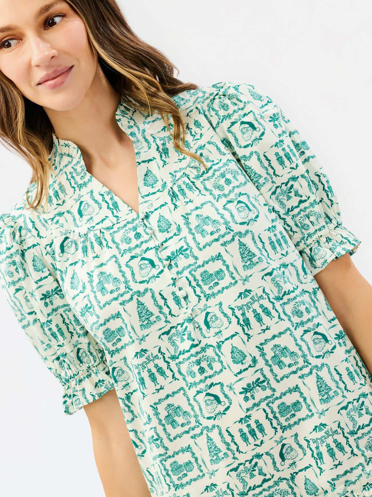 A woman wearing a short-sleeve collared blouse with a green and white geometric pattern, shown in a close-up studio shot against a light gray background.
