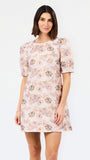 A woman modeling a short-sleeve puff-sleeve shift dress with a light pink base and a multicolor floral pattern, set against a plain white studio background.