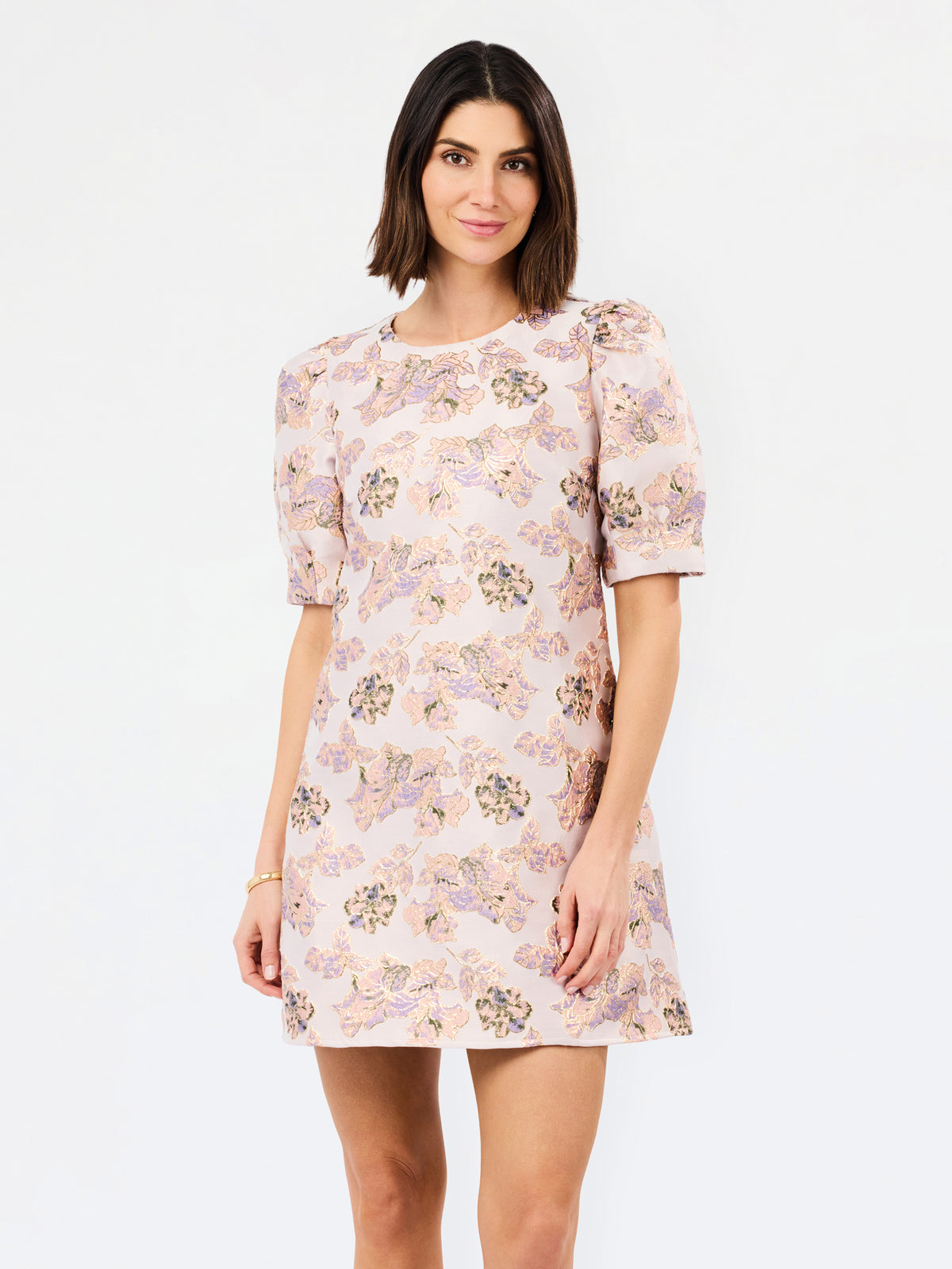 A woman modeling a short-sleeve puff-sleeve shift dress with a light pink base and a multicolor floral pattern, set against a plain white studio background.