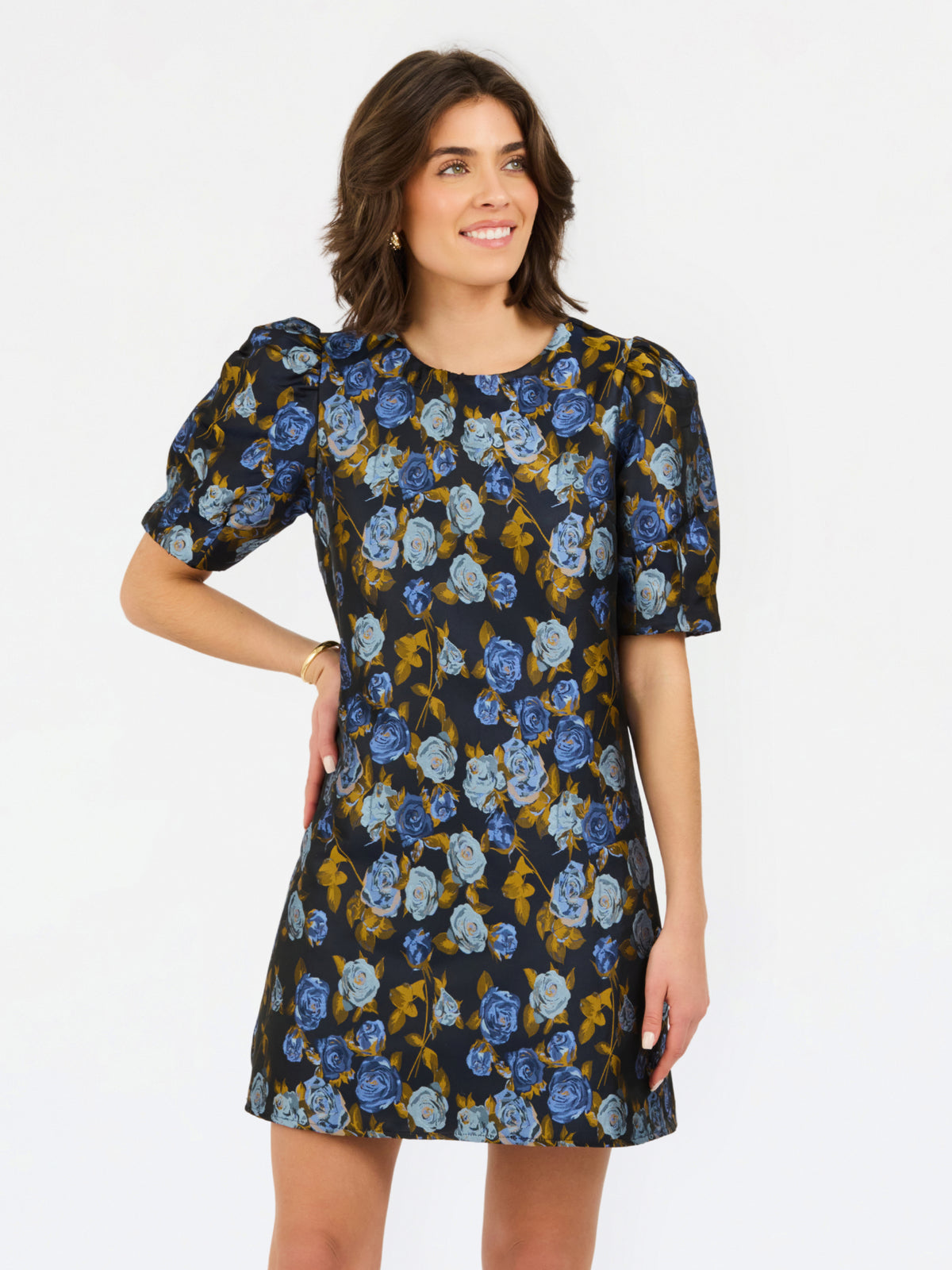 A woman modeling a short-sleeve A-line dress with a blue and mustard yellow floral print on a black background, set against a plain white studio background.