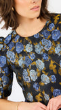 A close-up of a woman wearing a short-sleeve blouse with puff sleeves and a blue and light blue rose floral print on a black background.