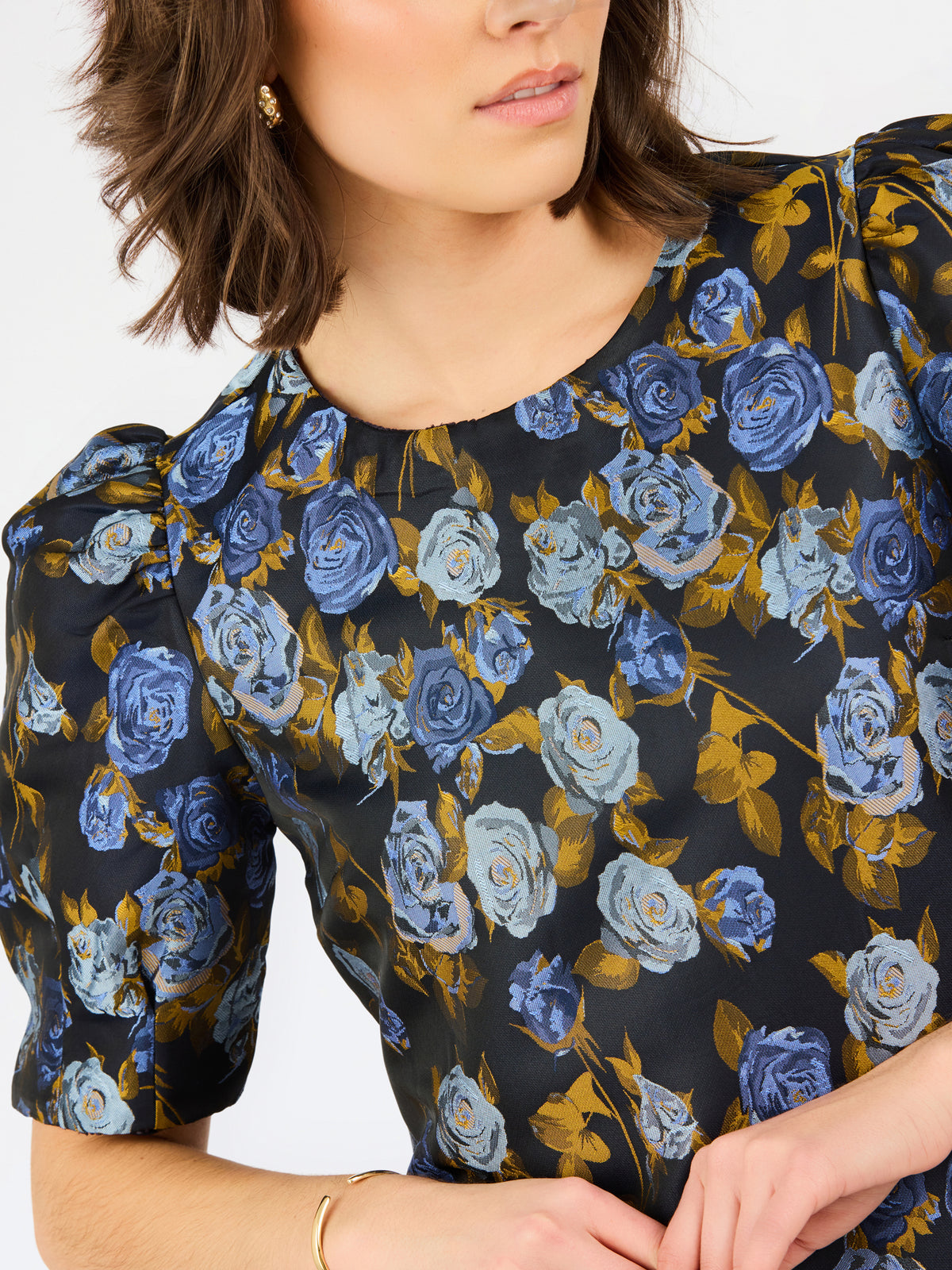 A close-up of a woman wearing a short-sleeve blouse with puff sleeves and a blue and light blue rose floral print on a black background.