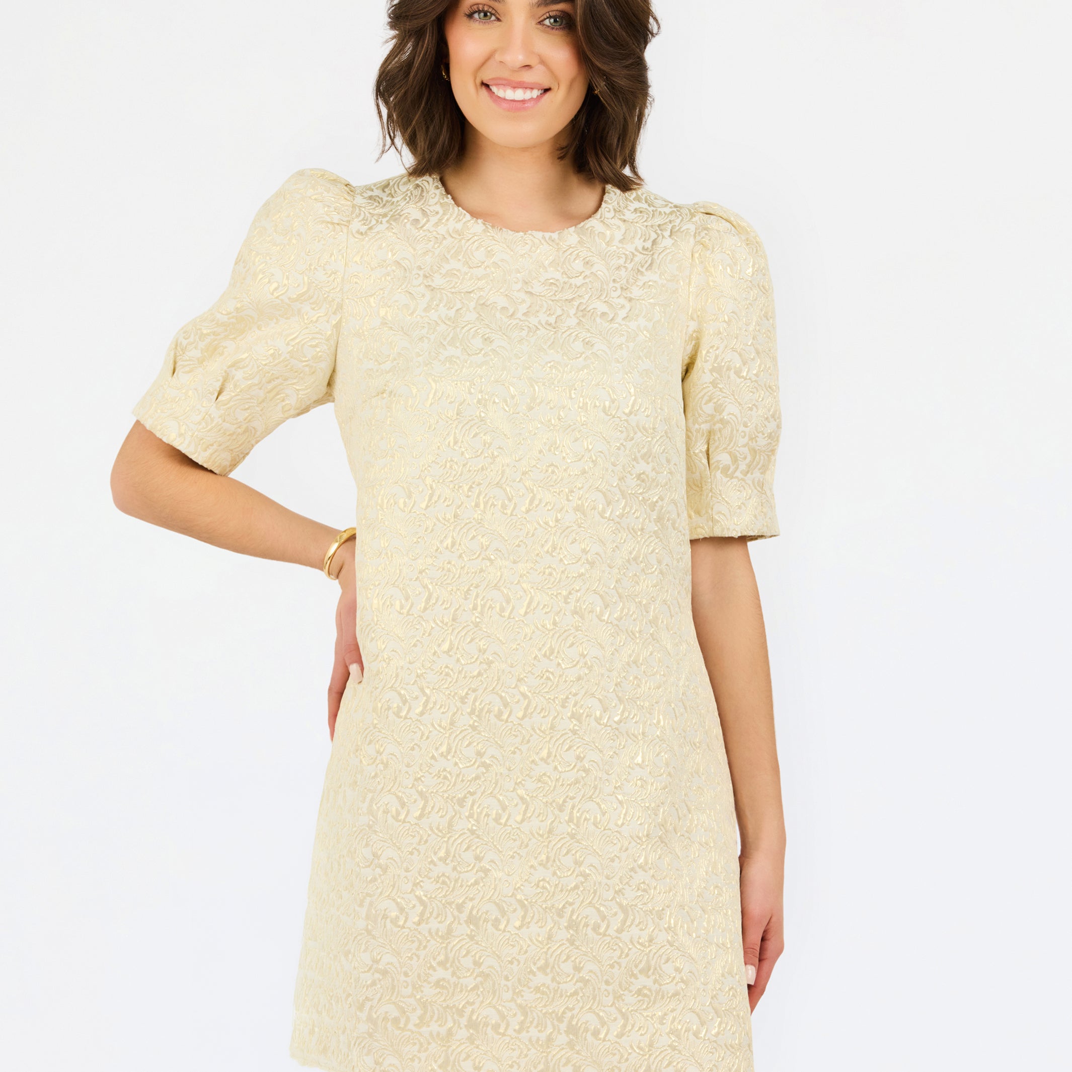 A woman modeling a short-sleeve cream lace dress with puff sleeves and a round neckline, photographed against a plain white studio background.