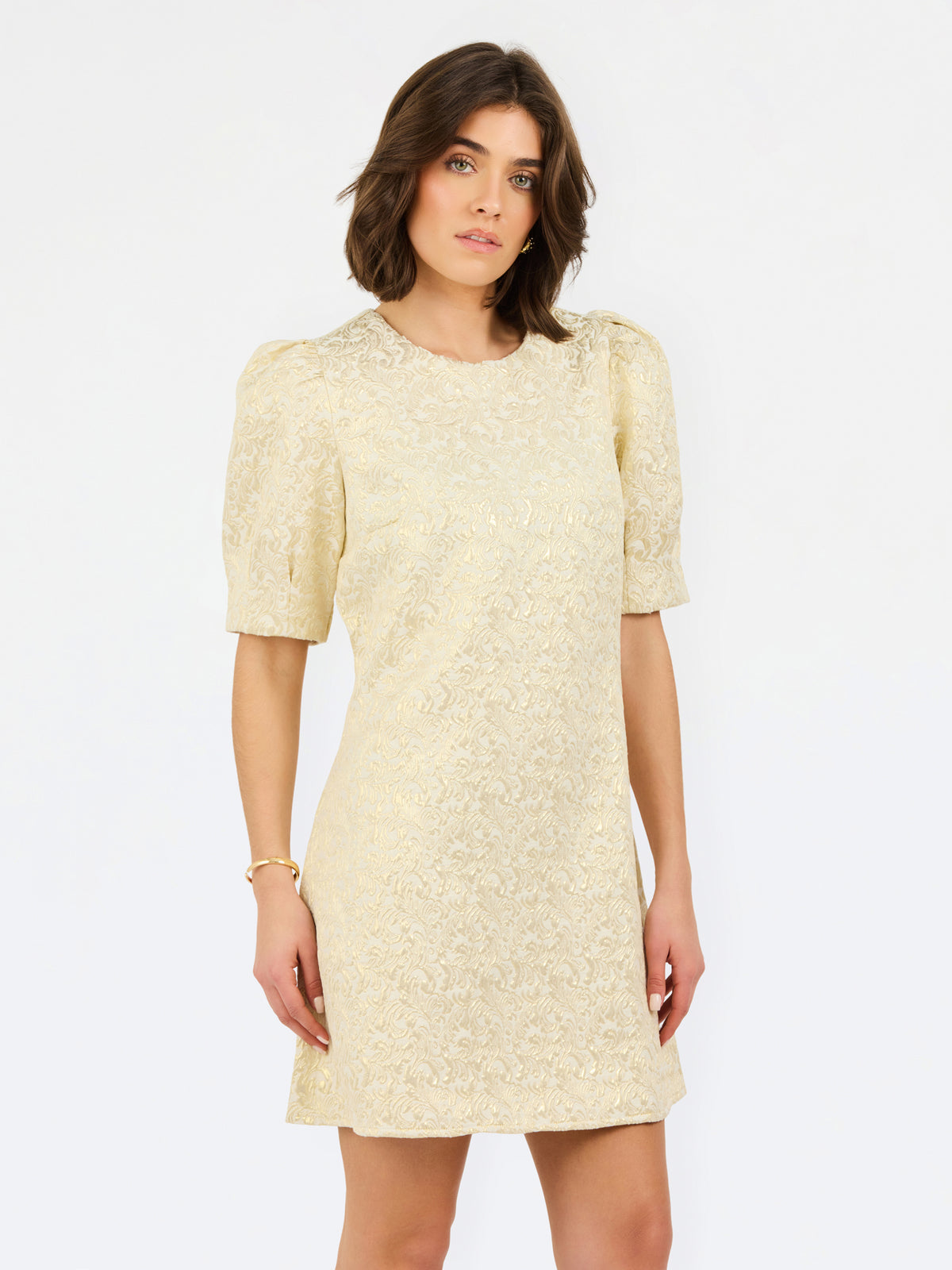 A woman modeling a short-sleeved cream lace dress with puff sleeves and a round neckline, set against a plain white studio background.