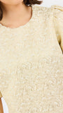 Close-up of a woman wearing a cream-colored textured top with a floral jacquard pattern and puffed short sleeves.