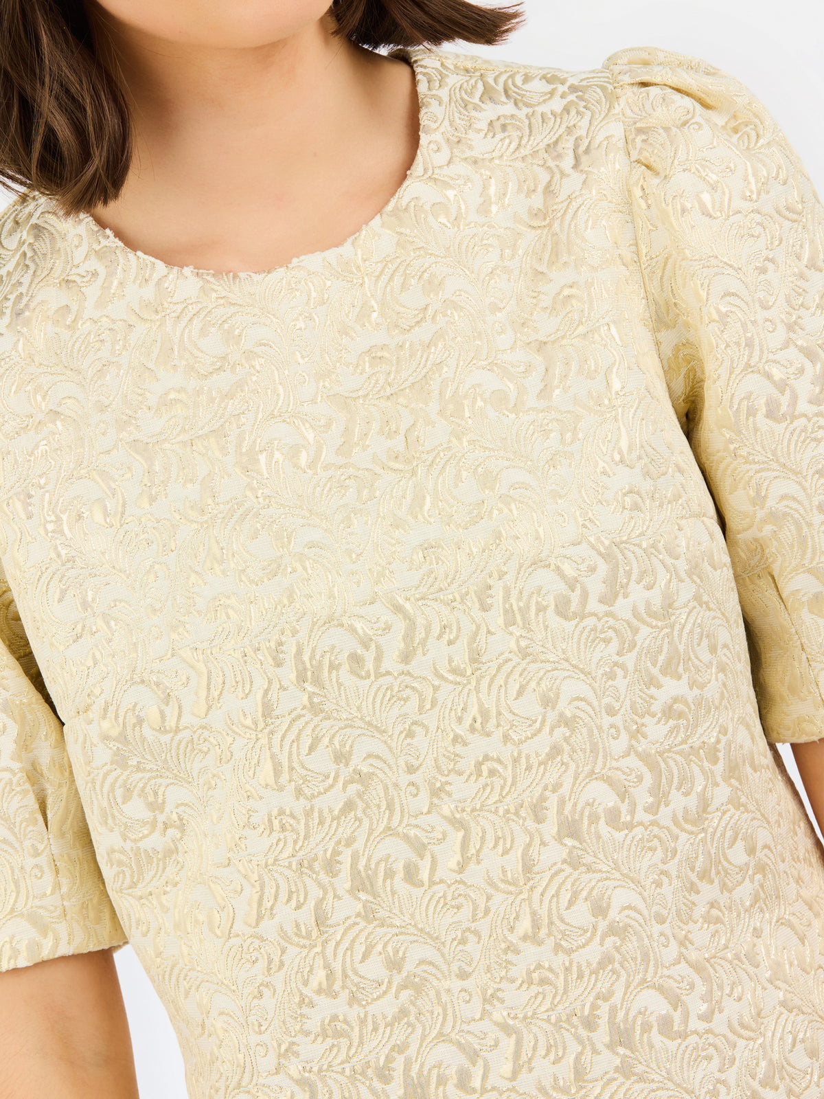 Close-up of a woman wearing a cream-colored textured top with a floral jacquard pattern and puffed short sleeves.