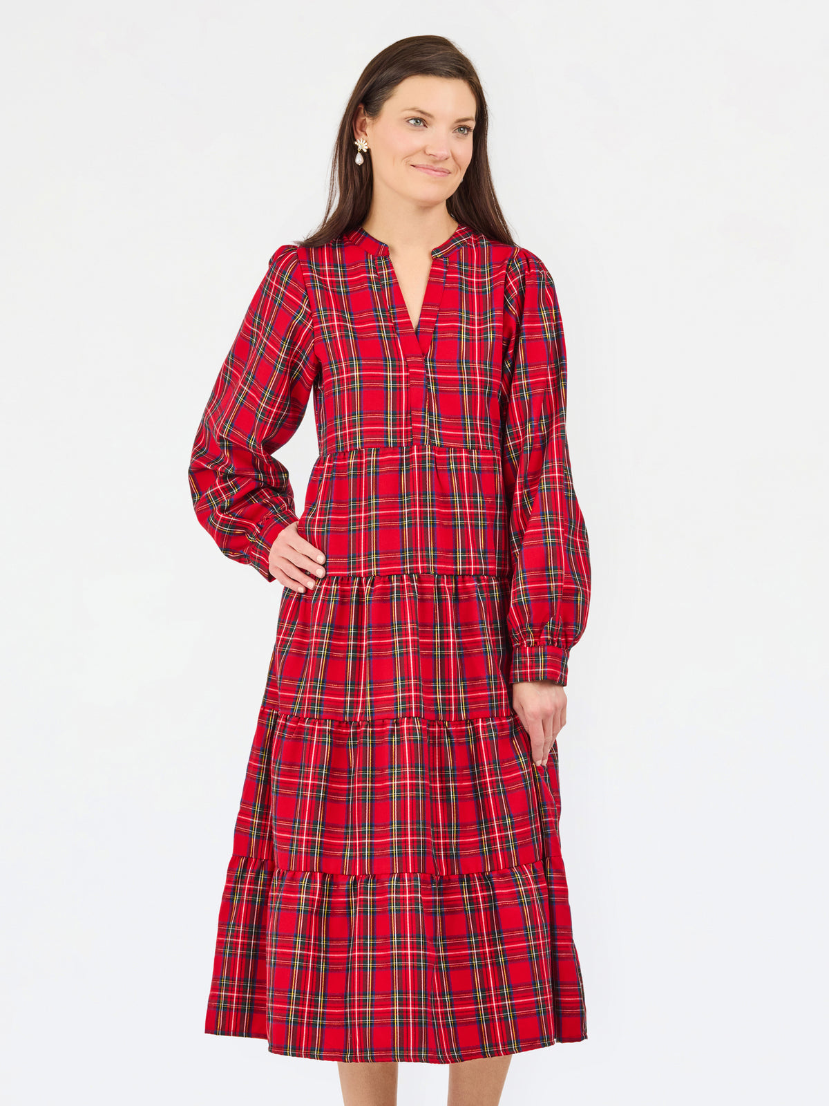 A woman modeling a red tartan plaid midi dress with tiered ruffles, long sleeves, and a split neckline, set against a plain white studio background.