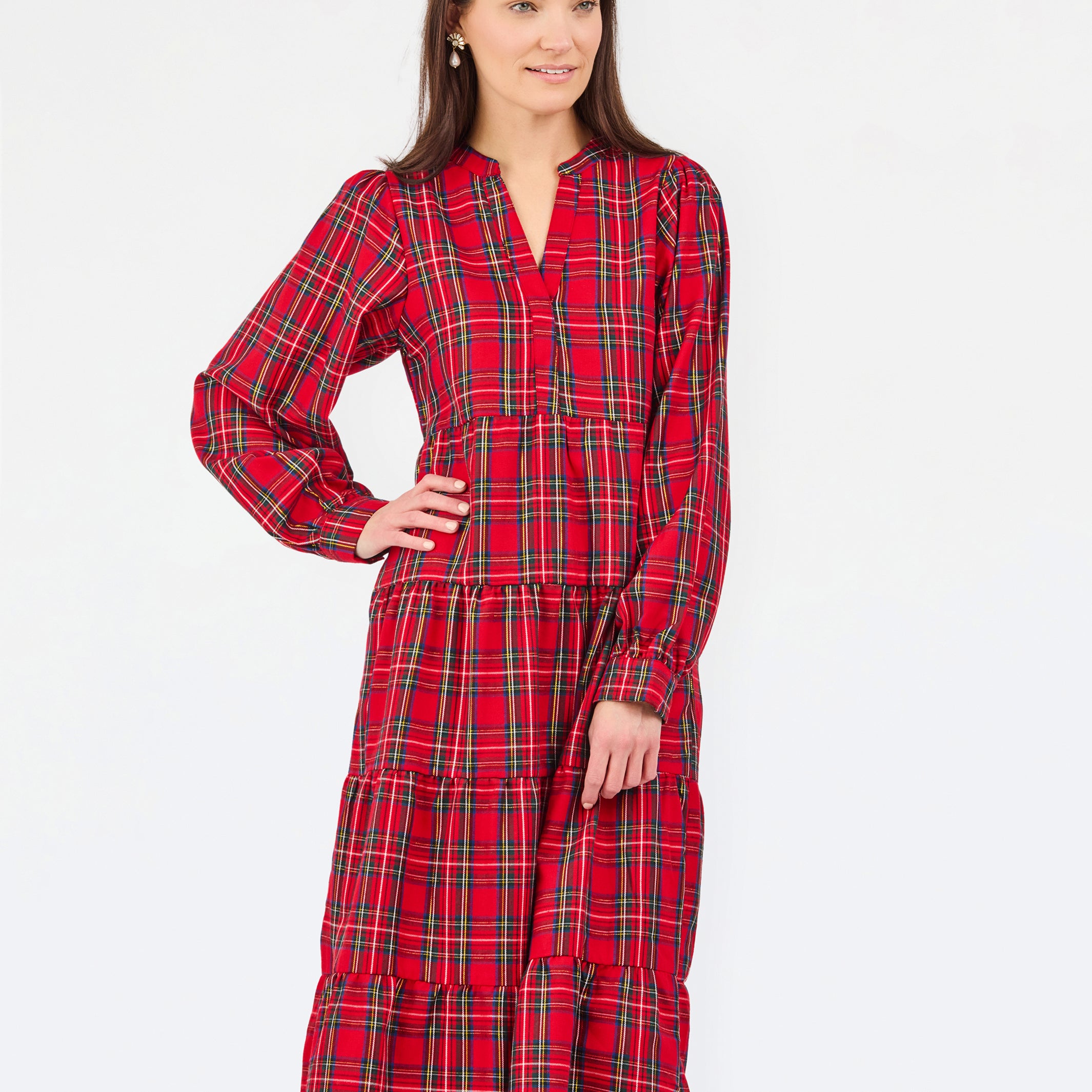 A woman modeling a red and black tartan plaid midi dress with long sleeves, a split neckline, and a tiered skirt, set against a plain white studio background.