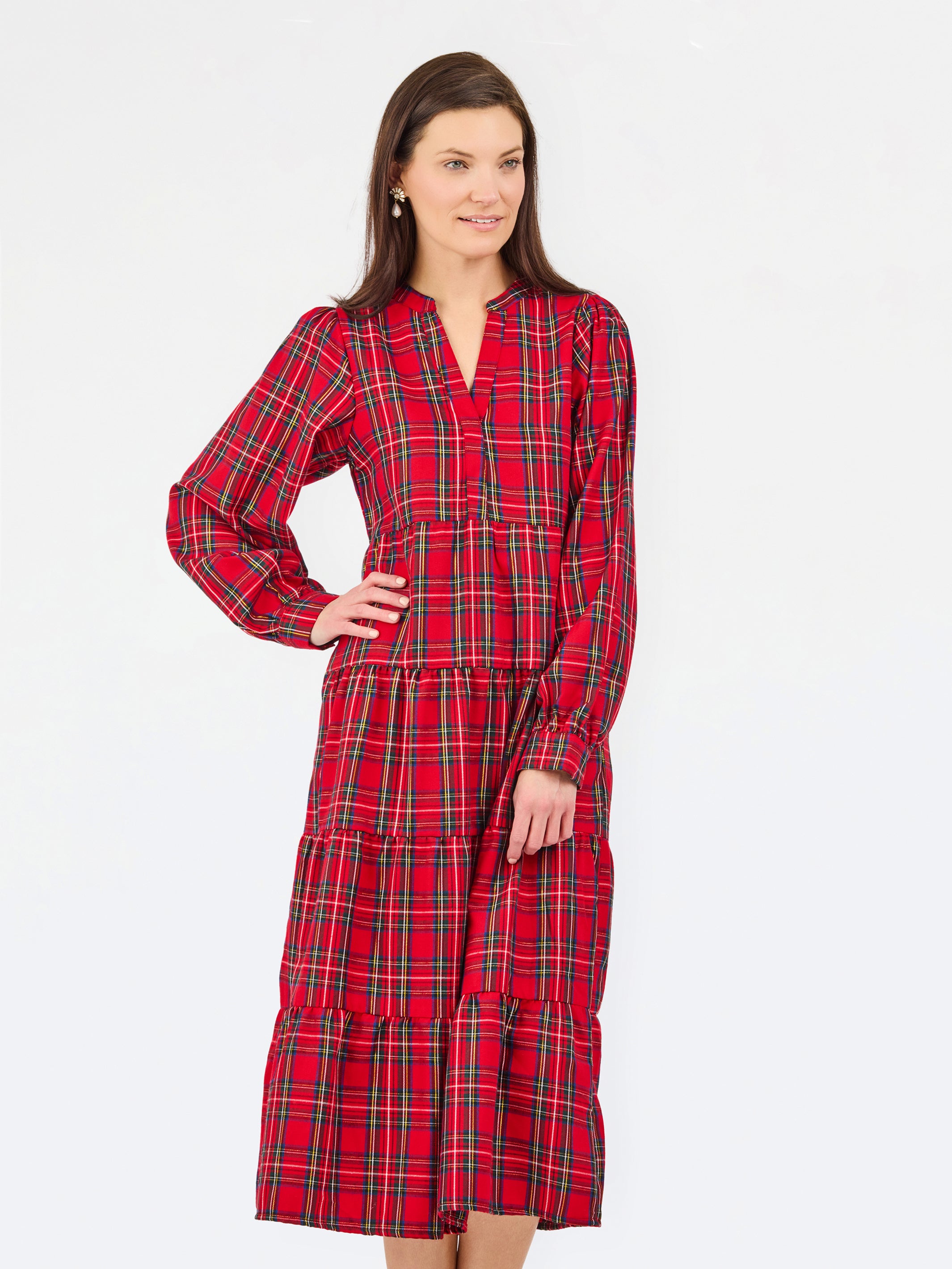 A woman modeling a red and black tartan plaid midi dress with long sleeves, a split neckline, and a tiered skirt, set against a plain white studio background.