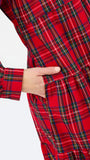 Close-up of a red tartan plaid dress with a hand tucked into a side pocket, against a plain white background.