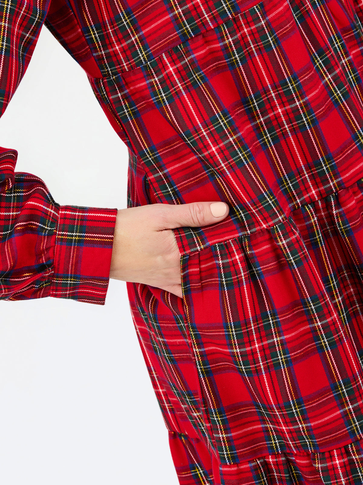 Close-up of a red tartan plaid dress with a hand tucked into a side pocket, against a plain white background.