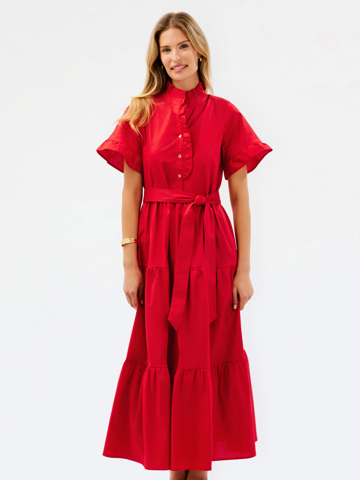 A woman modeling a bright red midi dress with short flutter sleeves, a high collar, buttoned front, and a matching waist tie, photographed against a plain white studio background.