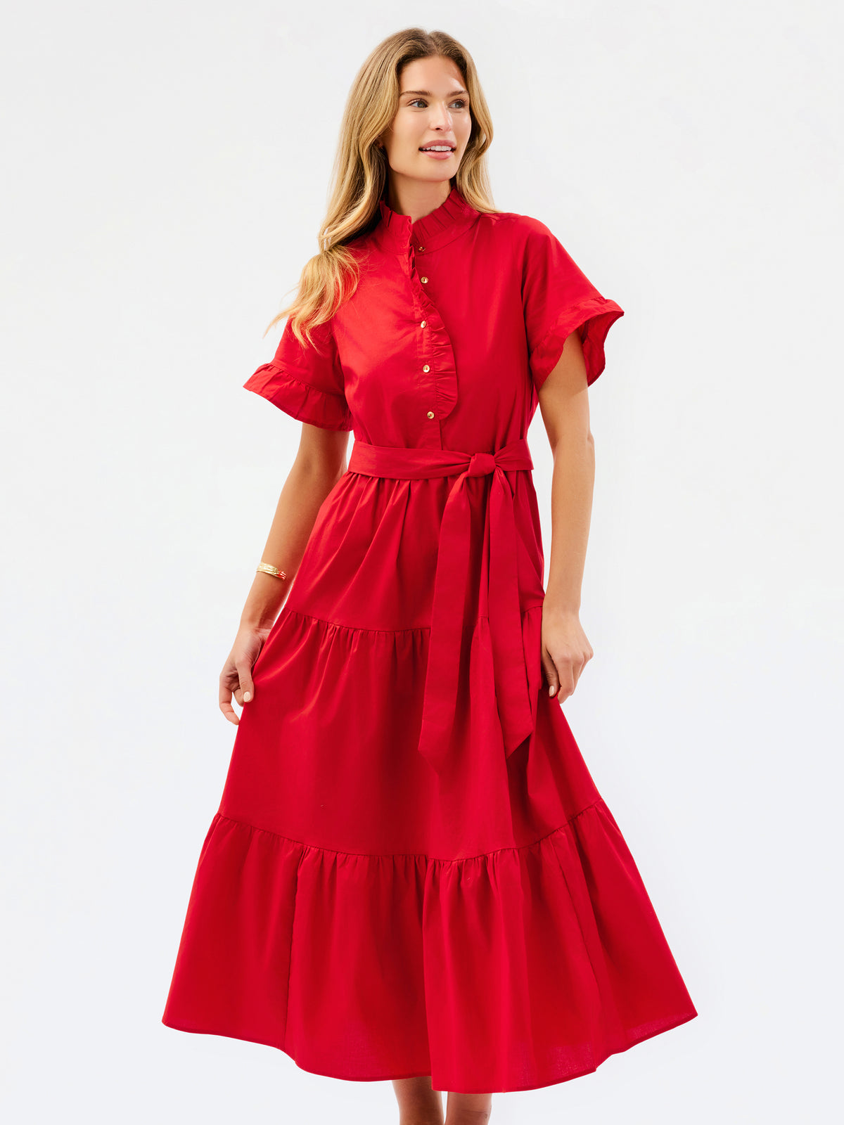 A woman modeling a bright red midi dress with short flutter sleeves, a buttoned stand collar, a matching waist tie, and a tiered skirt, photographed against a plain white studio background.