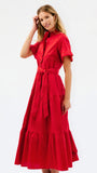 A woman modeling a bright red midi dress with short sleeves, a high collar, a button front, a matching waist tie, and a tiered skirt, photographed against a plain white studio background.