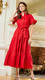 A woman modeling a bright red midi dress with short flutter sleeves, a button-front bodice, and a matching waist tie, posed in front of an ornate fireplace in a classical interior.