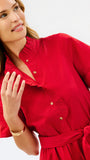 A close-up of a woman wearing a bright red short-sleeve shirt dress with ruffled trim, gold buttons, and a matching waist tie, against a clean white background.