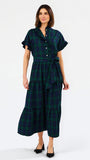 A woman modeling a dark green and black plaid midi shirt dress with short flutter sleeves, a button-up front, and a matching waist tie, paired with black heels against a plain white background.