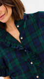Close-up of a woman wearing a green and navy plaid button-up shirt with ruffled trim and short sleeves.