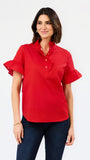 A woman modeling a bright red short-sleeve blouse with ruffled sleeves and a buttoned collar, paired with dark blue jeans, against a plain white studio background.