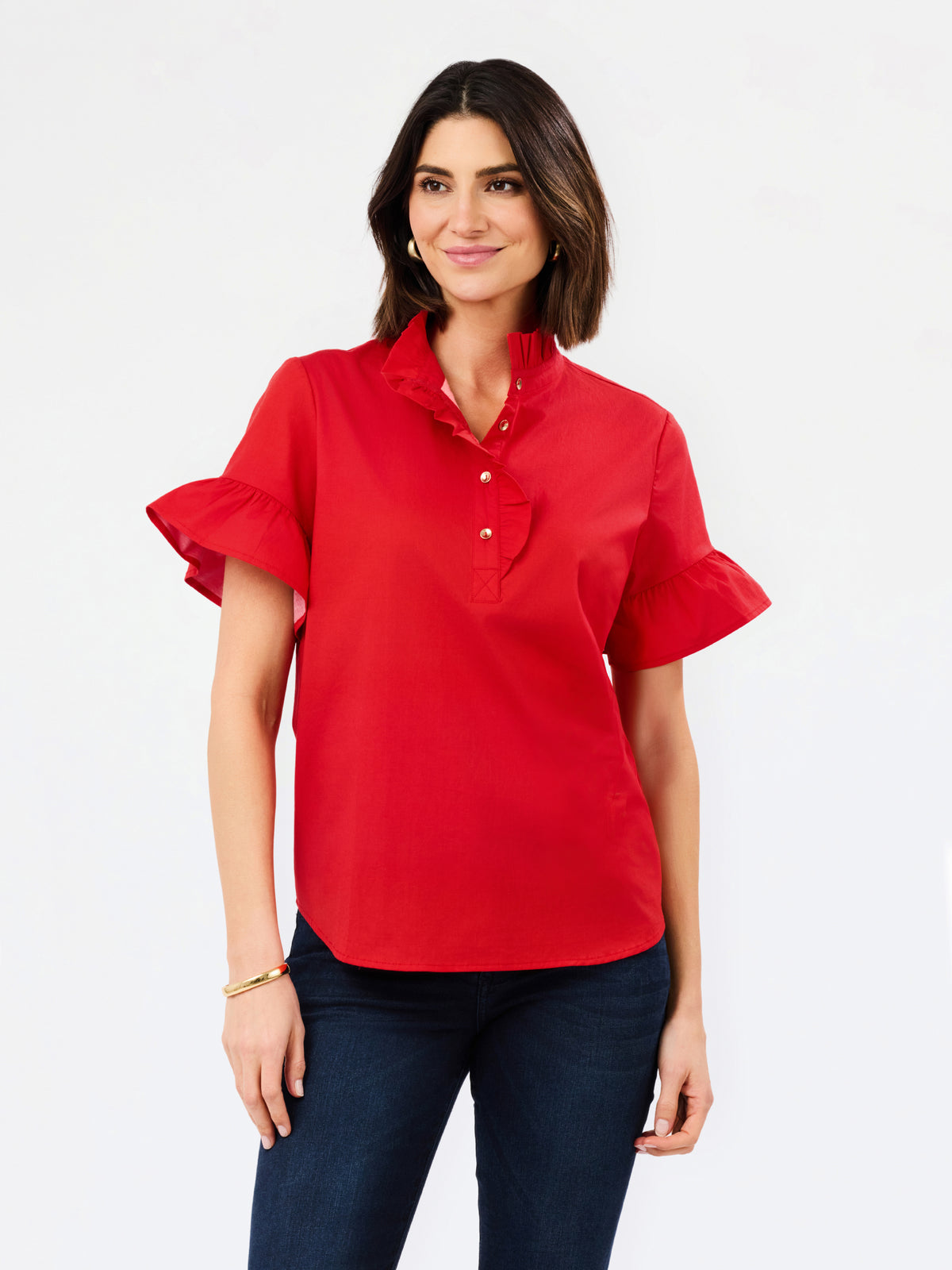 A woman modeling a bright red short-sleeve blouse with ruffled sleeves and a buttoned collar, paired with dark blue jeans, against a plain white studio background.