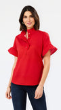 A woman modeling a bright red short-sleeve blouse with a high ruffled collar, button placket, and flutter sleeves, paired with dark blue jeans against a plain white studio background.