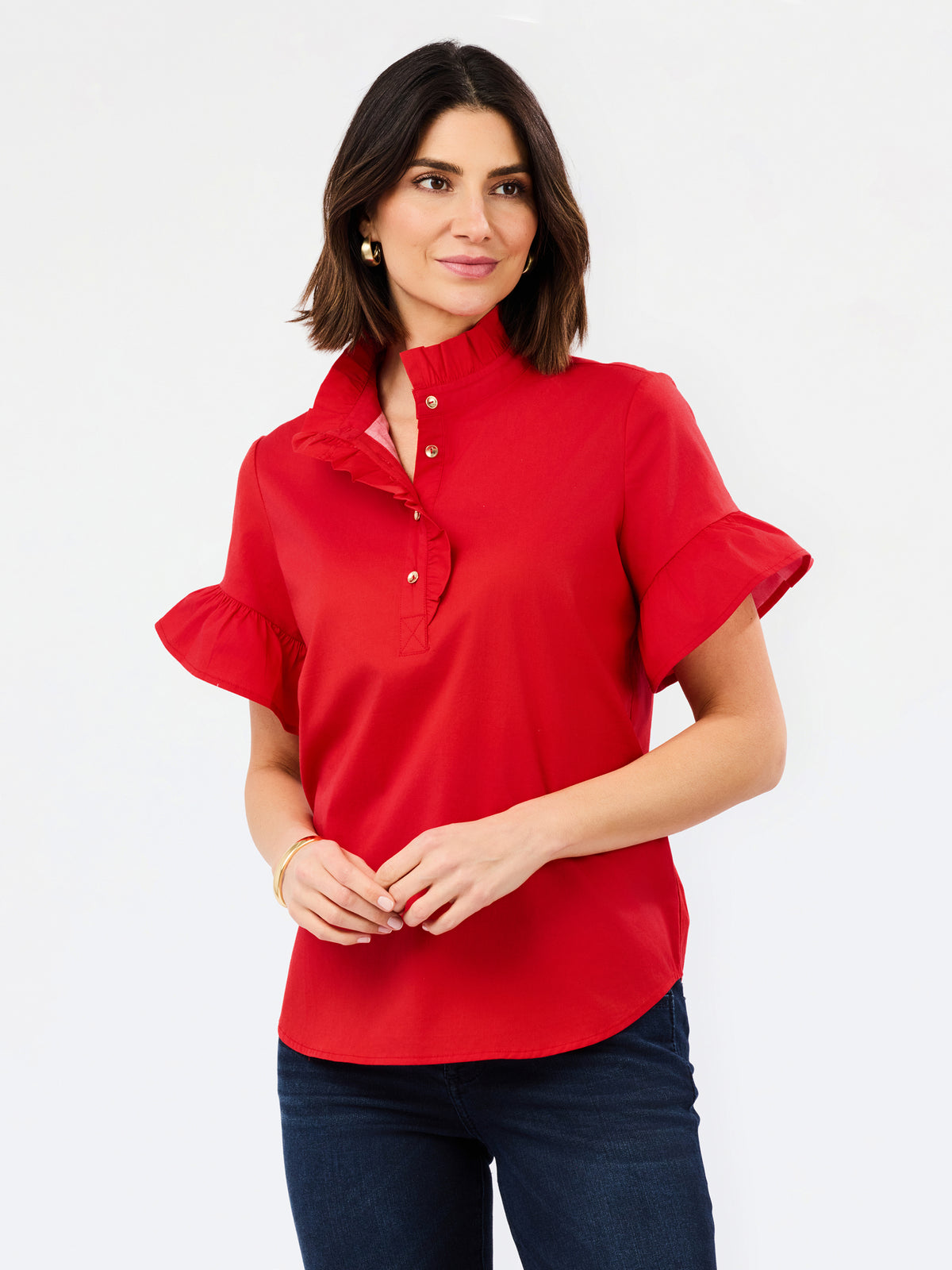 A woman modeling a bright red short-sleeve blouse with a high mock neck, button placket, and ruffled sleeves, paired with dark blue jeans against a plain white studio background.