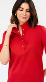A woman wearing a bright red short-sleeve blouse with a ruffled mock neck and gold buttons, photographed against a clean white studio background.
