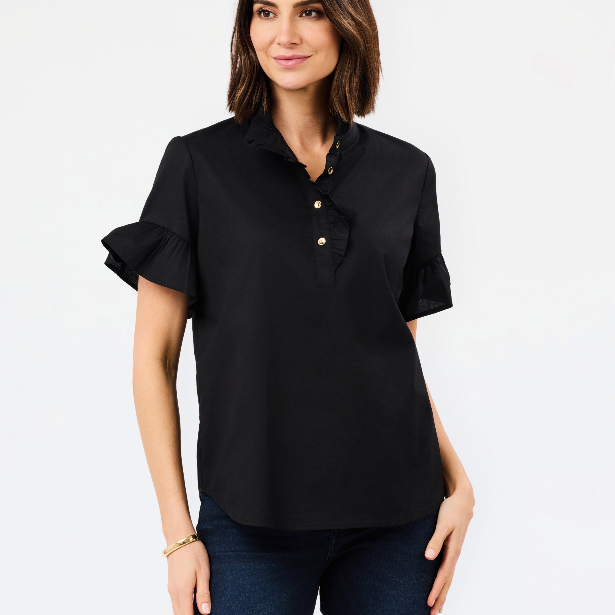 A woman modeling a black short-sleeve button-up blouse with ruffled sleeves and gold buttons, paired with dark blue jeans, against a plain white studio background.