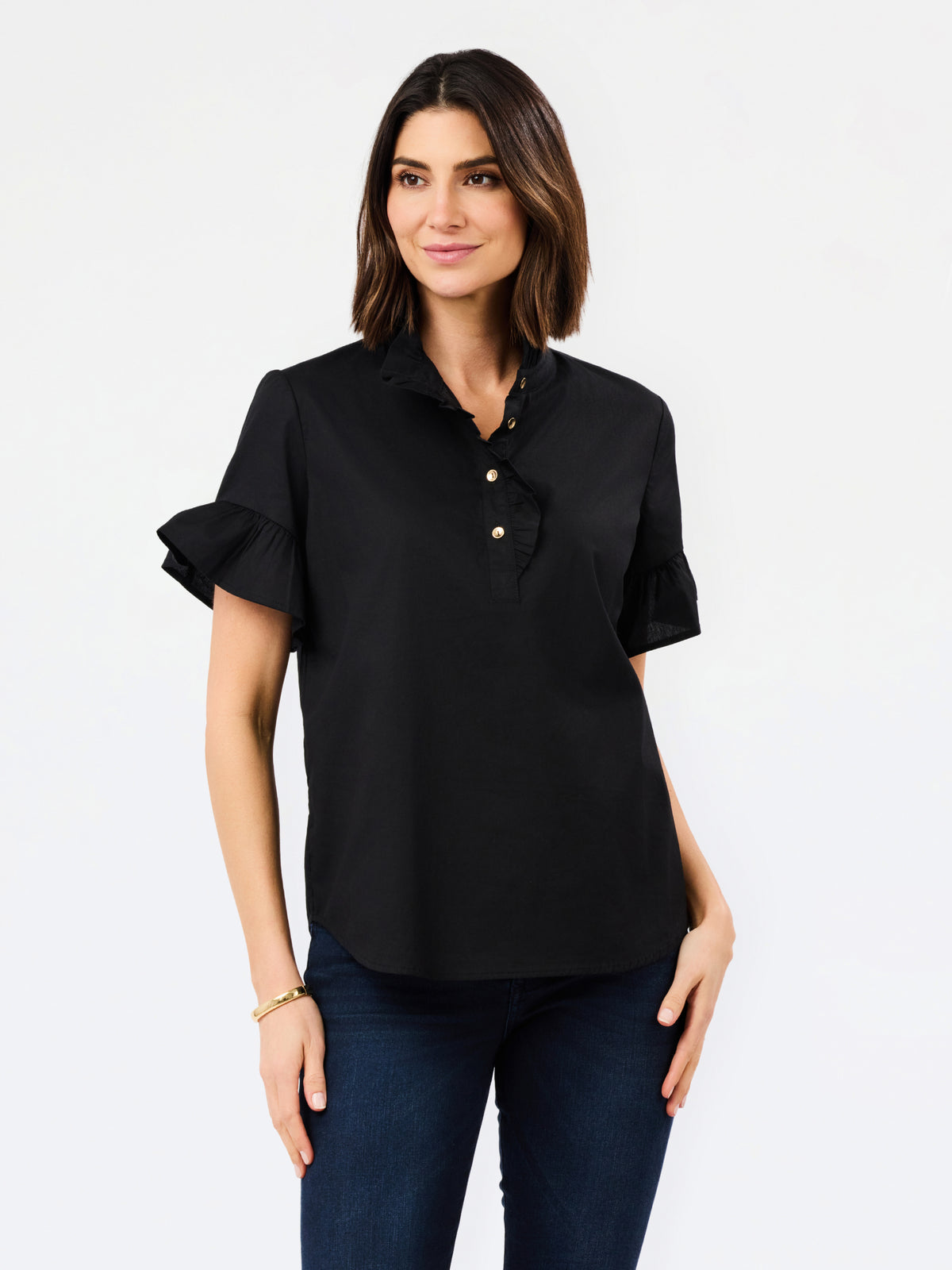 A woman modeling a black short-sleeve button-up blouse with ruffled sleeves and gold buttons, paired with dark blue jeans, against a plain white studio background.
