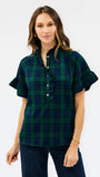 A woman modeling a short-sleeve button-front plaid blouse in dark green and navy with ruffled trim at the collar and sleeve cuffs, paired with dark jeans against a light gray studio background.