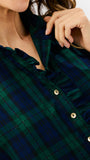Close-up of a woman wearing a dark green and navy plaid button-up blouse with ruffled trim and gold-tone buttons.