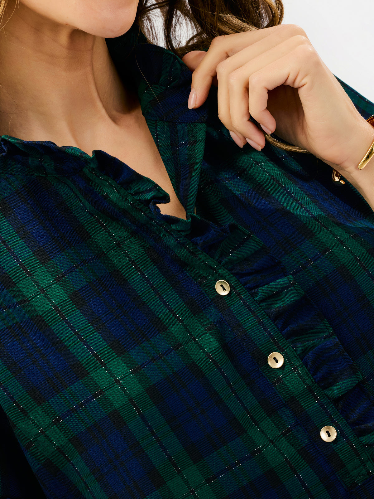 Close-up of a woman wearing a dark green and navy plaid button-up blouse with ruffled trim and gold-tone buttons.