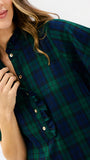 A close-up of a woman wearing a green and navy plaid button-up shirt with ruffled trim on the collar and placket, styled with gold buttons.